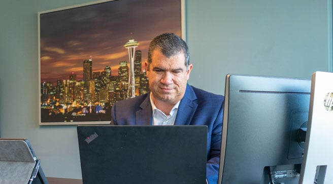public storage divisional manager greg at at his desktop at his office with photo of seattle skyline in the background